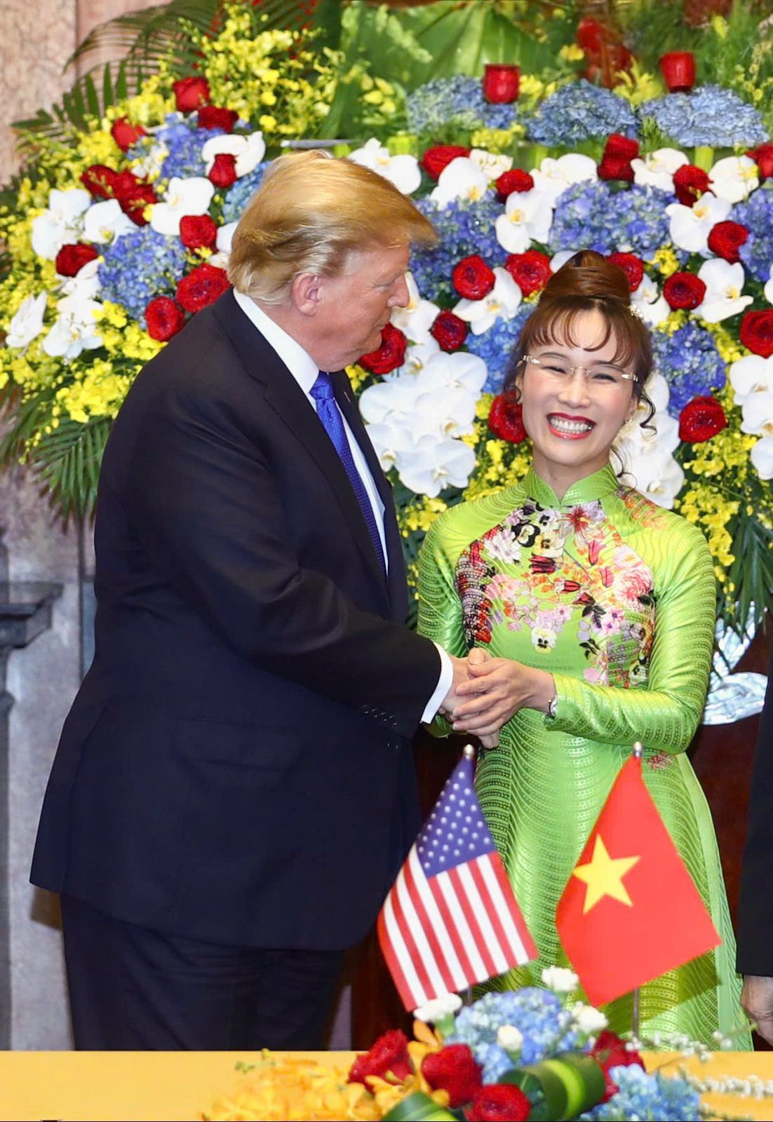 A person in a suit shaking hands with a person in a green dressDescription automatically generated